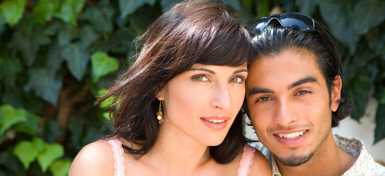 Smiling couple standing close together outdoors in front of green ivy