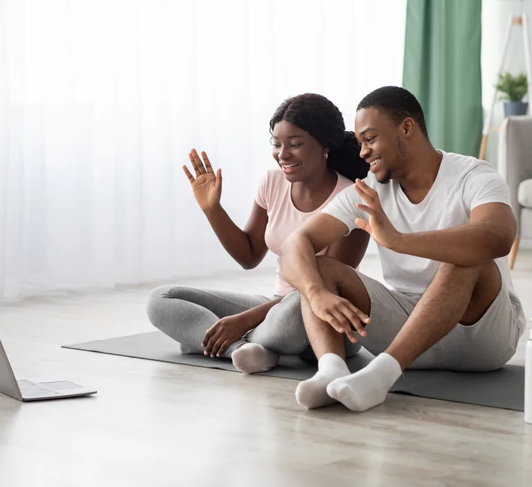 Couple waving at a laptop during an online couples therapy session at home