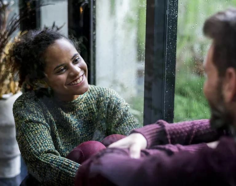 Couple sitting close by a rainy window, talking and reconnecting