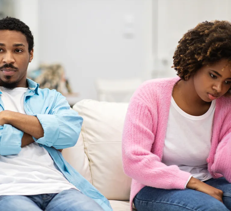 Couple sitting apart and disconnected on a couch, looking upset